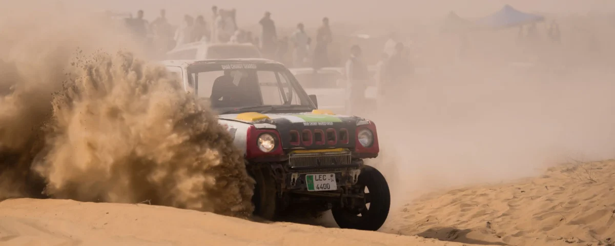 Wide shot of an off-road racing vehicle speeding across the vast golden sand dunes of the Dubai desert.