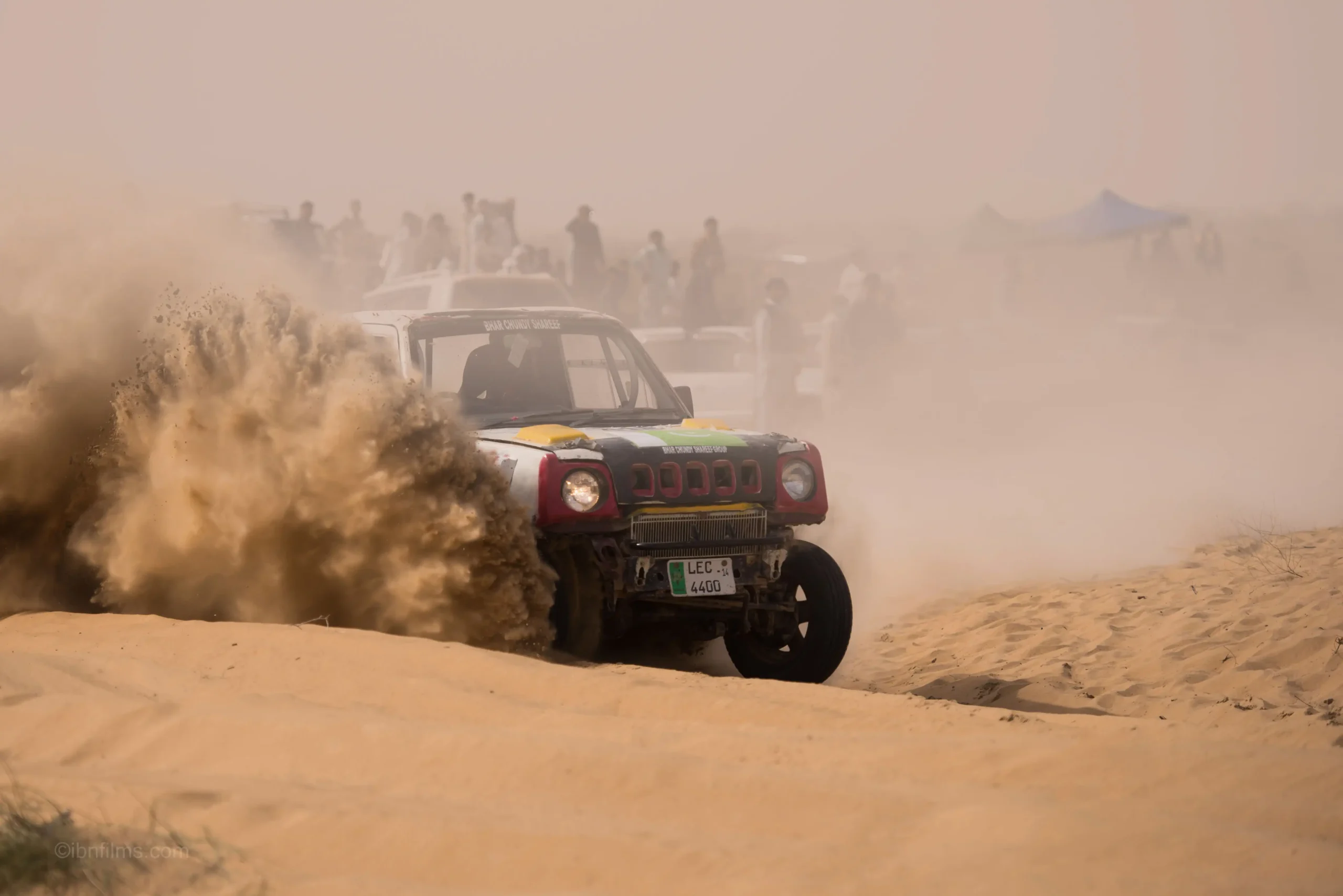 Wide shot of an off-road racing vehicle speeding across the vast golden sand dunes of the Dubai desert.