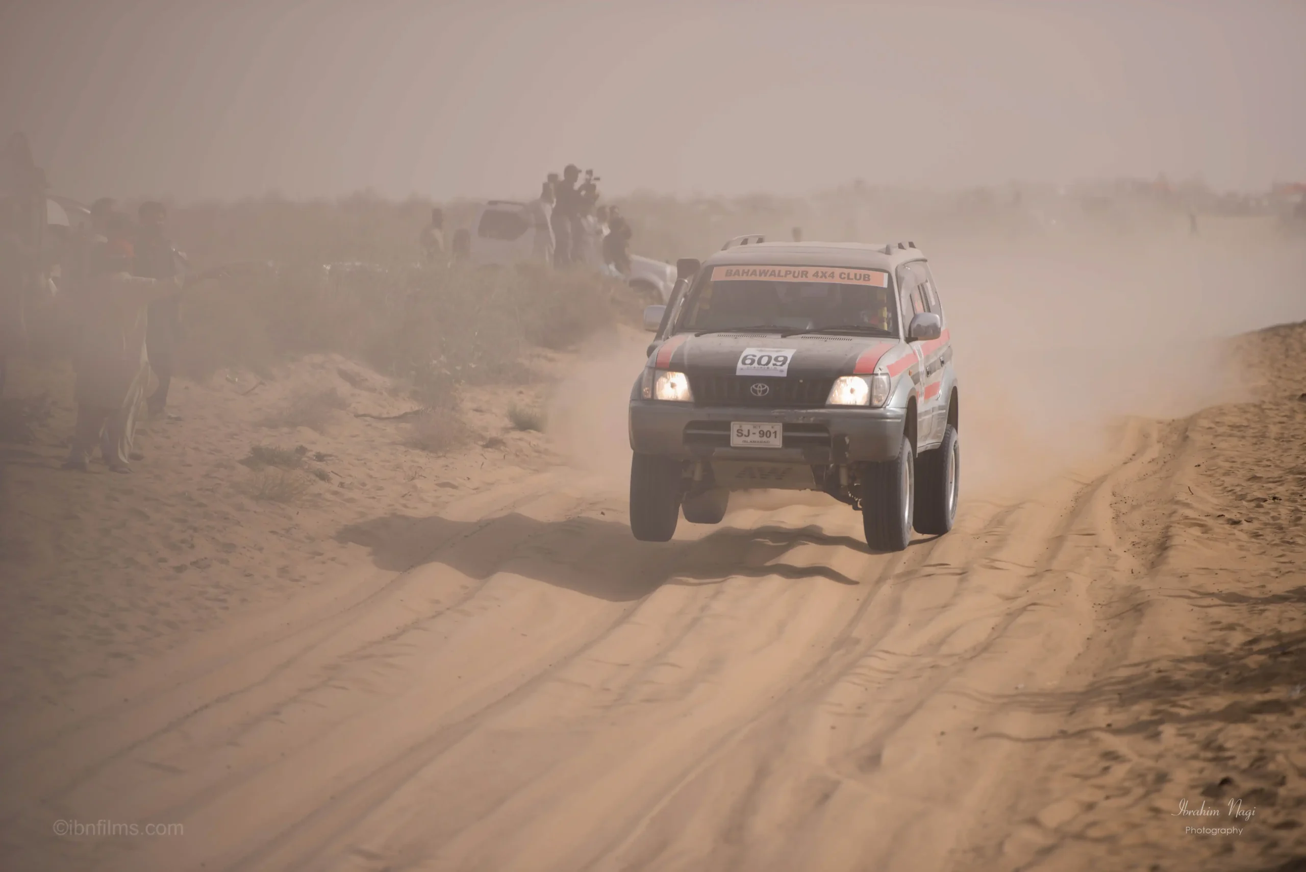 A high-performance racing motorcycle kicking up sand while speeding through the Dubai desert dunes at sunset.