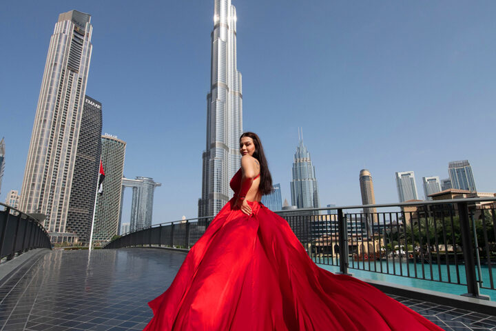 Fashion editorial photography in Dubai UAE featuring a model in a long red gown posing in front of Burj Khalifa